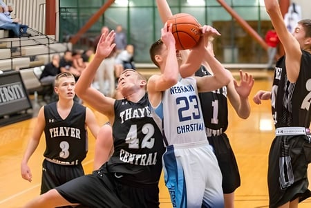 Schüler der Nebraska Christian Schools spielen Basketball auf dem Spielfeld mit Zuschauern im Hintergrund.