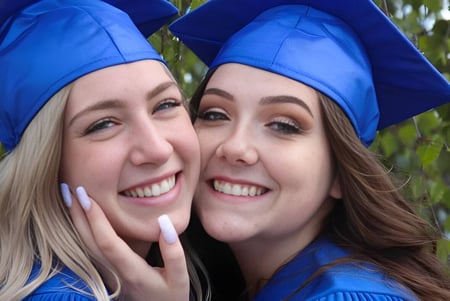 Zwei Schülerinnen der Nechako Valley Secondary School in blauen Abschlussroben posieren gemeinsam vor einer unscharfen Naturkulisse.