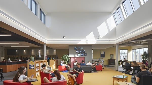 Schüler und Schülerinnen der Nelson High School sitzen in der hellen Lobby auf roten Sesseln und arbeiten an Laptops oder unterhalten sich.