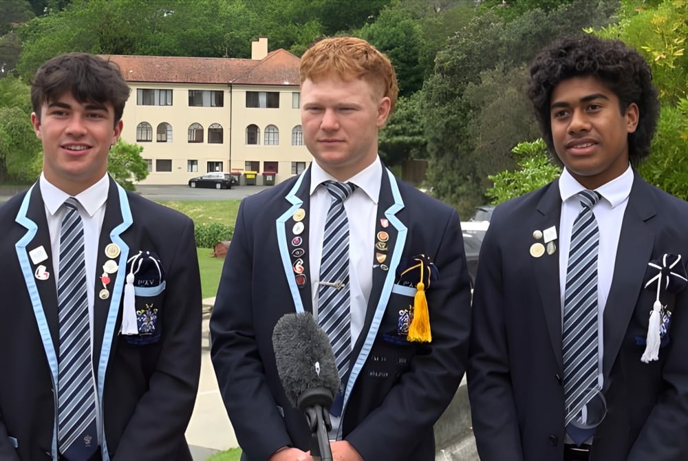 Drei Schüler der Nelson College for Boys stehen vor einem Gebäude mit grünem, bewaldetem Hintergrund.