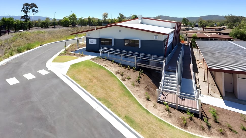 Das moderne zweistöckige Gebäude der Nerang State High School steht auf einem grasbewachsenen Hügel mit Bergen im Hintergrund.