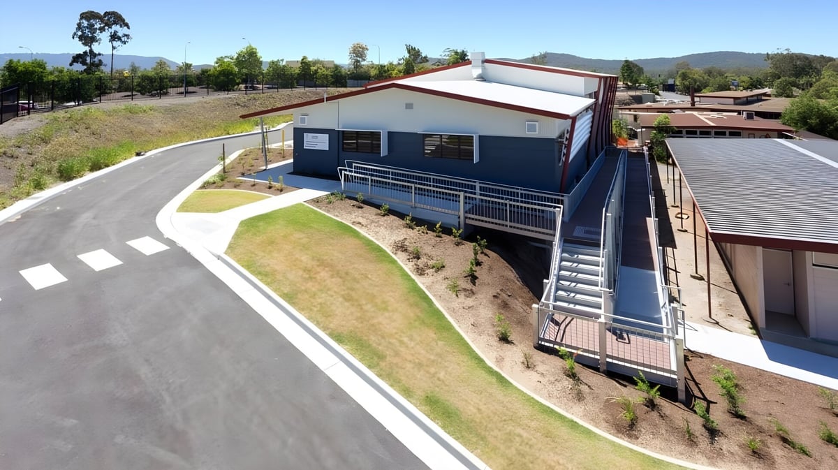 Das moderne zweistöckige Gebäude der Nerang State High School steht auf einem grasbewachsenen Hügel mit Bergen im Hintergrund.