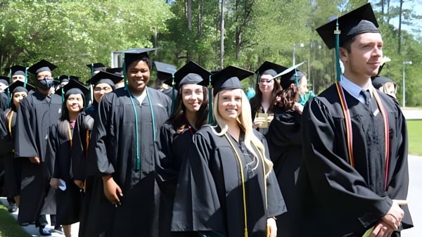 Eine Gruppe von Absolventinnen und Absolventen der New Brunswick Community College steht in akademischer Kleidung in einem bewaldeten Außenbereich zusammen.