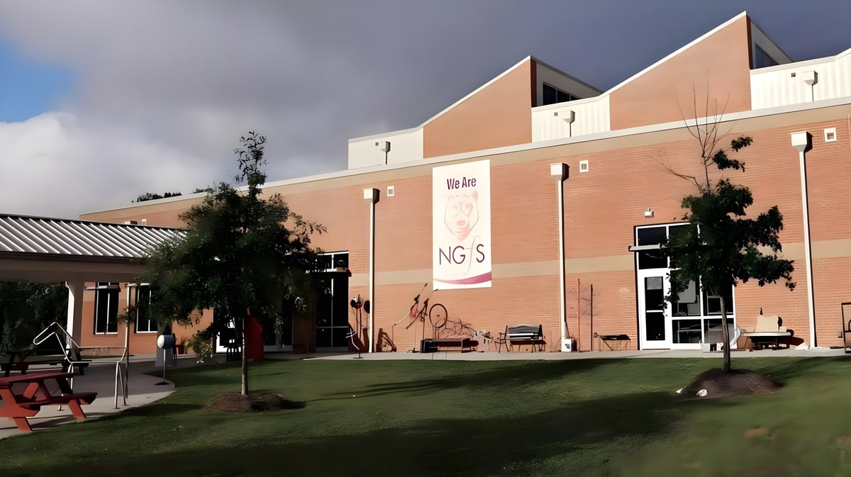 Das orangefarbene Gebäude der New Garden Friends School steht vor einer Wiese mit Bänken und Bäumen.