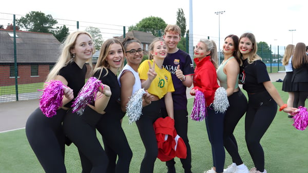 Eine Gruppe junger Schülerinnen posiert gemeinsam auf dem Sportfeld der New Hall School mit Schulgebäude und Bäumen im Hintergrund.