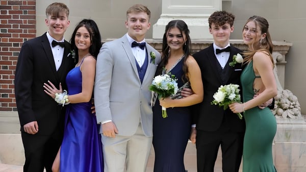 Eine Gruppe formell gekleideter Schülerinnen und Schüler steht vor einem Backsteingebäude der New Hampton School.