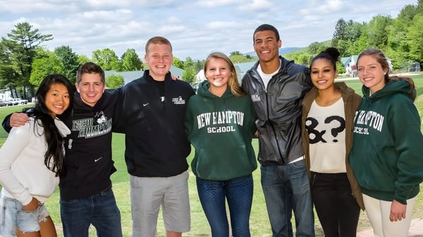 Eine Gruppe Schülerinnen und Schüler steht draußen auf einer Wiese auf dem Campus der New Hampton School.