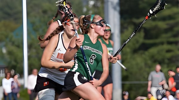 Zwei Lacrosse-Spielerinnen der New Hampton School kämpfen auf dem Spielfeld um den Ball vor Zuschauern.