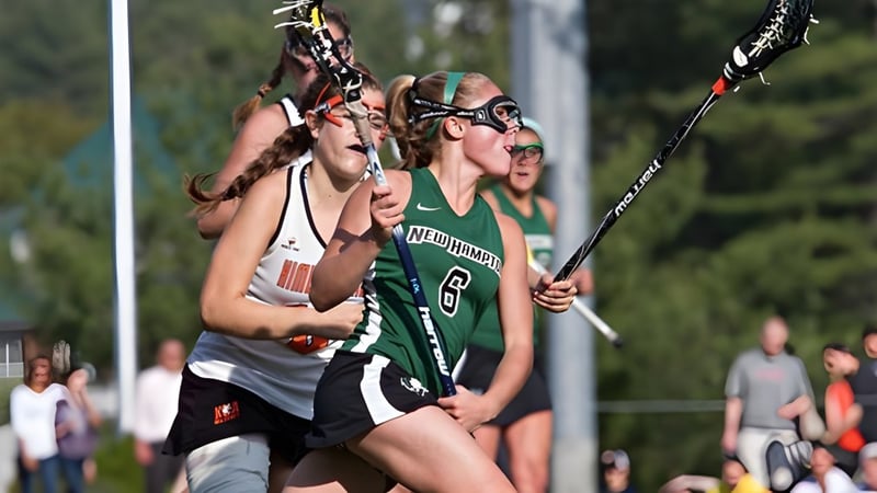 Zwei Lacrosse-Spielerinnen der New Hampton School kämpfen auf dem Spielfeld um den Ball vor Zuschauern.