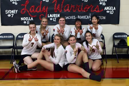 Eine Gruppe junger Athletinnen posiert auf dem Basketballfeld der New Hope Christian School vor einem Banner mit dem Teamnamen.