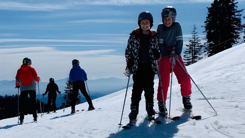 Eine Gruppe von Schülern der New Hope Christian School fährt Ski auf einem verschneiten Berghang mit Kiefern und blauem Himmel im Hintergrund.