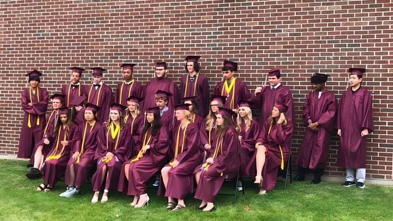 Absolventinnen und Absolventen der N.E.W. Lutheran High School stehen in ihren Talaren vor einer Backsteinwand und feiern ihren Abschluss.