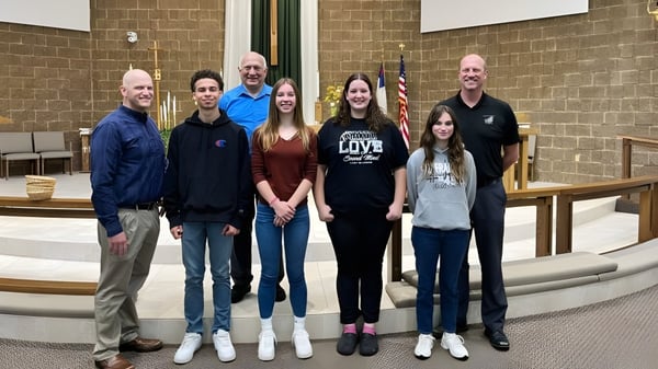 Schüler und Erwachsene stehen vor dem Backsteingebäude der N.E.W. Lutheran High School mit einer amerikanischen Flagge.