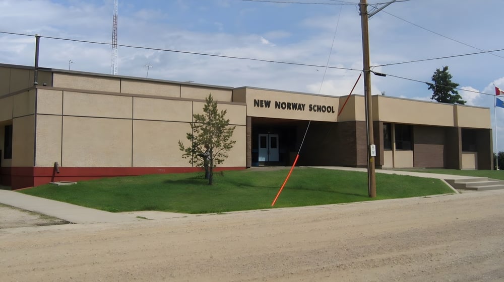 Das moderne Schulgebäude der New Norway School mit Rasenfläche und einem unbefestigten Weg im Vordergrund unter blauem Himmel.