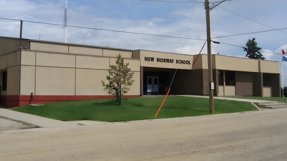 Das moderne Schulgebäude der New Norway School mit einem Grasfeld im Vordergrund und Stromleitungen im Hintergrund.