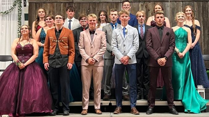 Eine Gruppe formell gekleideter Schülerinnen und Schüler der New Norway School posiert vor einer Holzstruktur.