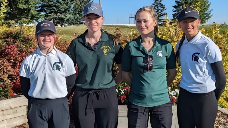 Vier Schülerinnen und Schüler der New Norway School in Michigan State University Sportbekleidung stehen vor einem bewaldeten Hintergrund unter klarem blauen Himmel.