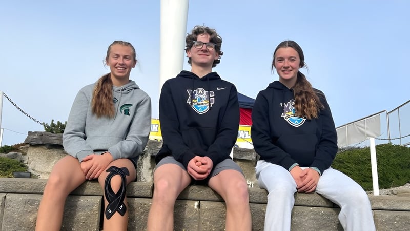 Drei Schüler sitzen auf einer Mauer im Freien vor blauem Himmel auf dem Campus der New Norway School.