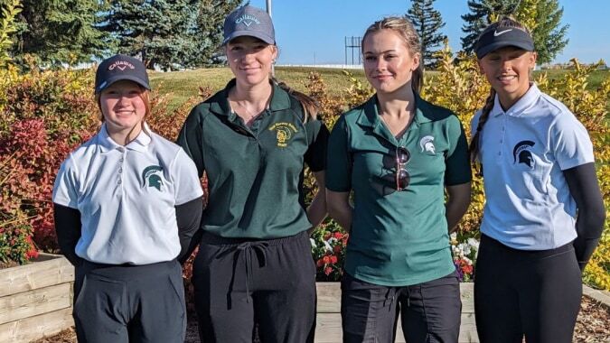 Eine Gruppe von vier Schülern der New Norway School in Sportbekleidung steht gemeinsam in einem natürlichen Außenbereich mit Bäumen.