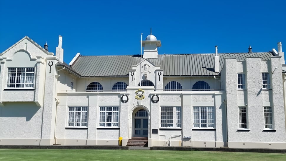 Das imposante Hauptgebäude der New Plymouth Boys' High School steht vor klarem blauem Himmel und gepflegtem Rasen.