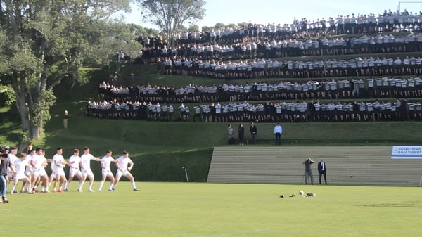 Eine große Gruppe von Schülern der New Plymouth Boys' High School versammelt sich auf einer Wiese vor einer hohen, dicht bepackten Struktur.