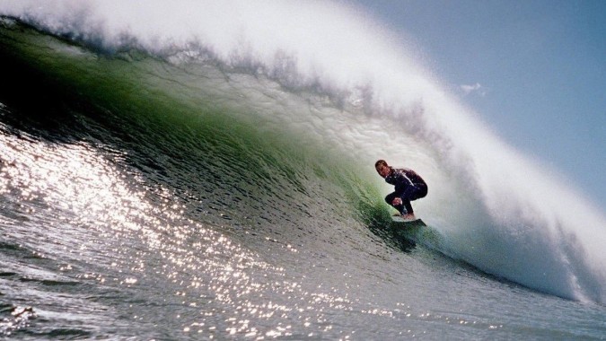 Ein Schüler der New Plymouth Boys' High School surft auf einer großen Welle vor klarem blauem Himmel.