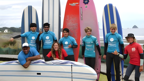 Schüler der New Plymouth Boys' High School posieren mit Surfboards vor einer Küstenlandschaft mit Bergen im Hintergrund.