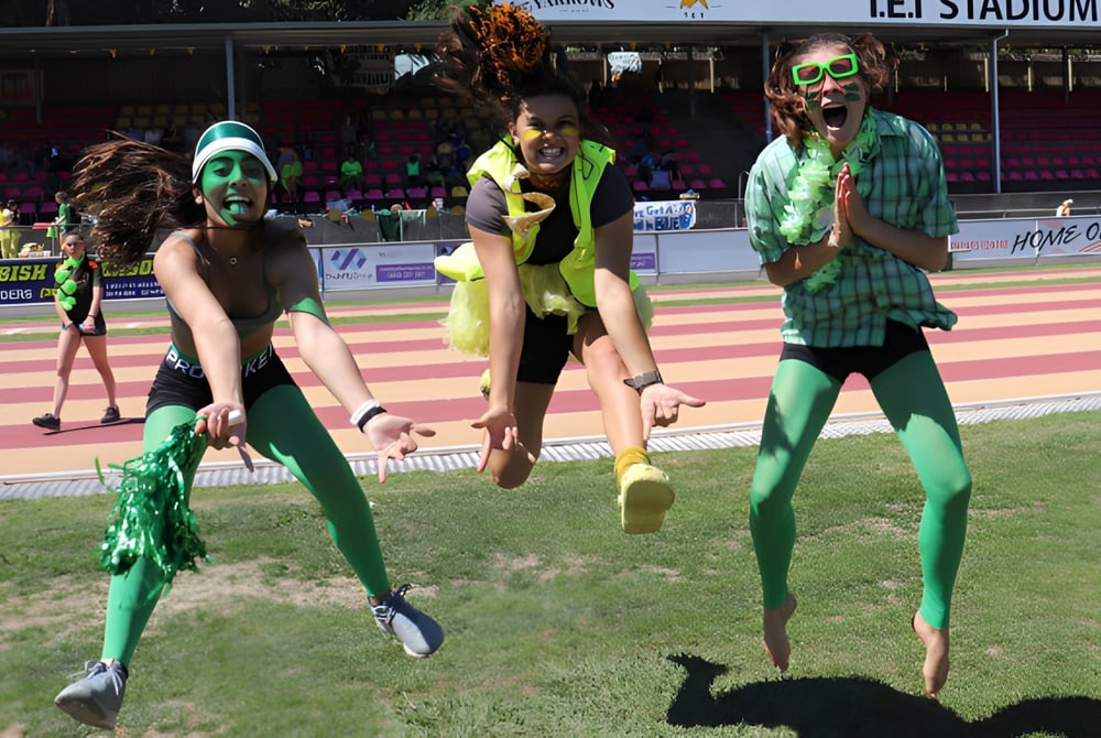 Schülerinnen der New Plymouth Girls’ High School posieren in bunten Kostümen auf einem Sportfeld vor dem Stadion.