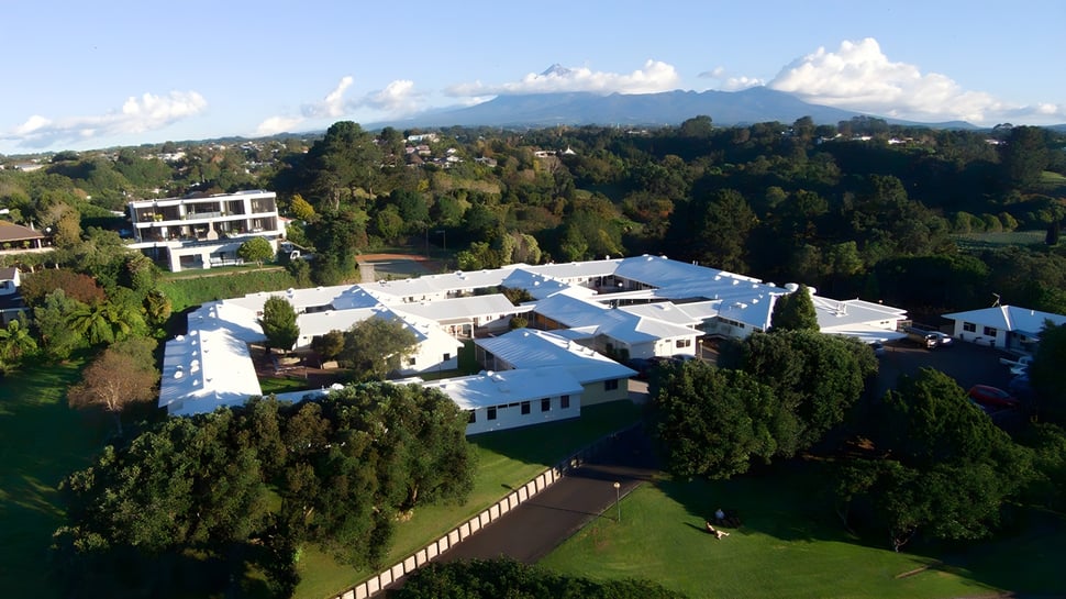 Ein weitläufiges Wohngebäude vor Bergen und blauem Himmel auf dem Campus der New Plymouth Girls’ High School.