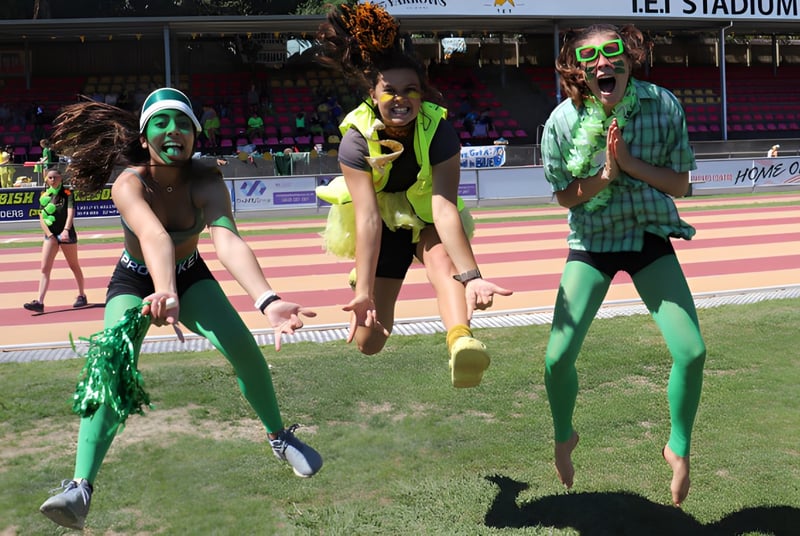 Eine Gruppe von Schülerinnen der New Plymouth Girls’ High School steht in bunten Kostümen auf einem Sportfeld mit Stadion im Hintergrund.