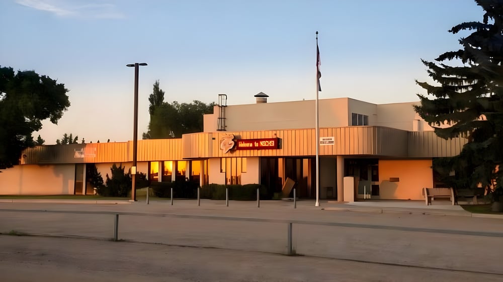 Das moderne orangefarbene Gebäude der New Sarepta Community High School ist von Bäumen umgeben und steht unter klarem Himmel.