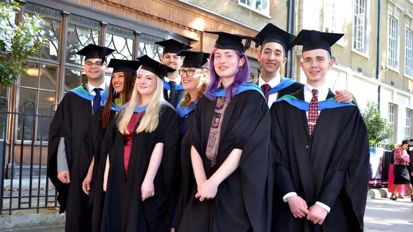 Eine Gruppe von Absolventen steht vor einem Backsteingebäude auf dem Campus der New Westminster Secondary School.