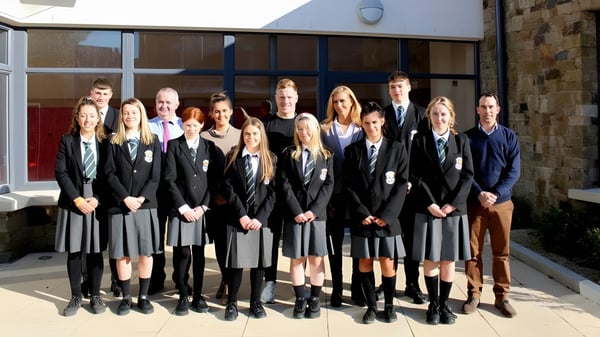Eine Gruppe von Schülerinnen und Schülern des Newbridge College in Abschlusstracht steht vor einem Gebäude.