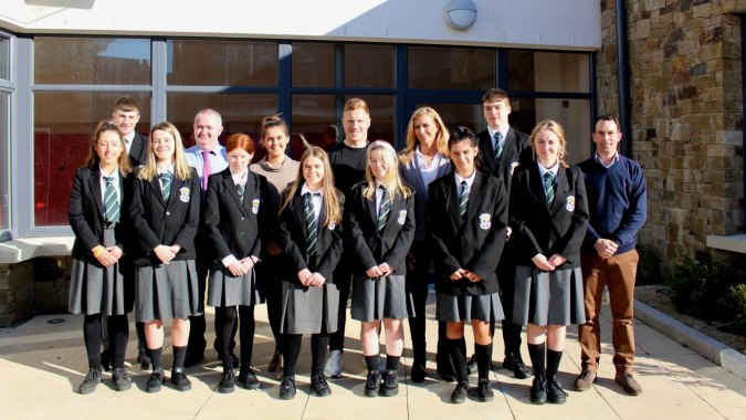 Eine Gruppe von Absolventinnen und Absolventen des Newbridge College steht vor einem Gebäude mit Steinfassaden und großen Fenstern.