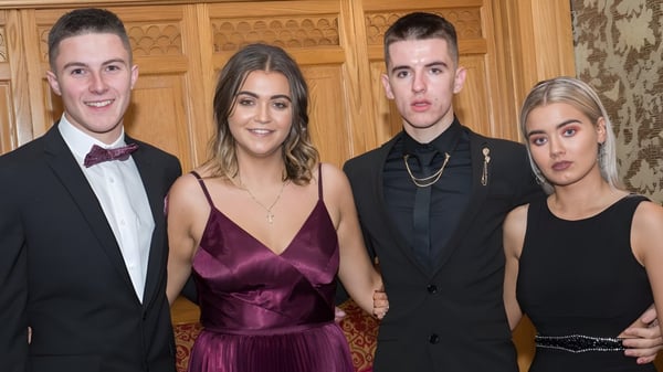 Vier gut gekleidete Personen posieren gemeinsam in einem reich verzierten Holzraum auf dem Campus des Newbridge College.