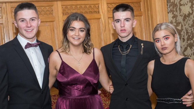 Vier gut gekleidete Personen posieren zusammen in einem verzierenden Holzraum auf dem Campus des Newbridge College.