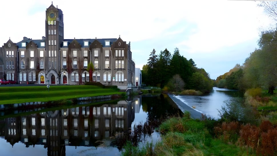 Das historische Gebäude des Newbridge College mit einem hohen Uhrturm spiegelt sich im ruhigen Wasser eines Kanals wider.