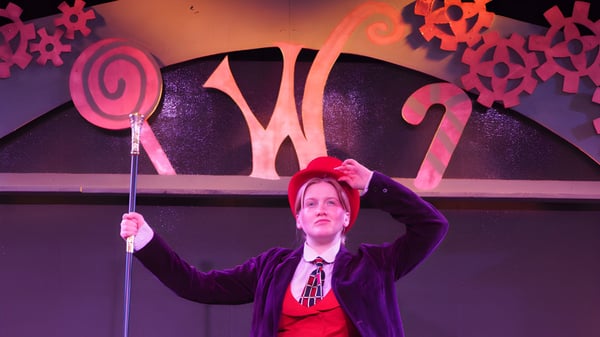 Eine Person in lila Kleidung steht vor der bunten, abstrakten Bühnenkulisse auf dem Campus der Newcastle High School.