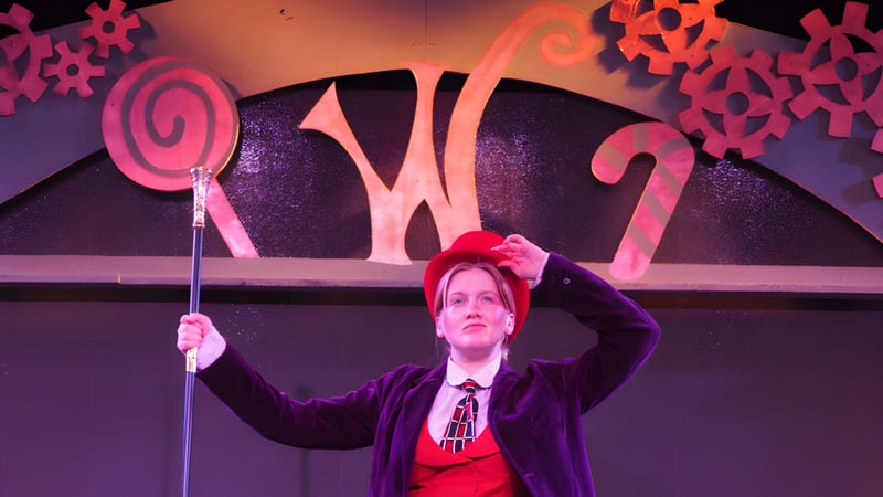 Eine Person in lila Kleidung steht vor der bunten, abstrakten Bühnenkulisse auf dem Campus der Newcastle High School.