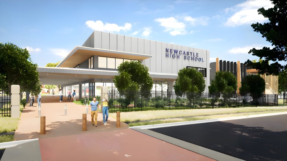 Das moderne zweistöckige Schulgebäude der Newcastle High School mit Eingang, Bäumen und gepflastertem Weg im Vordergrund.