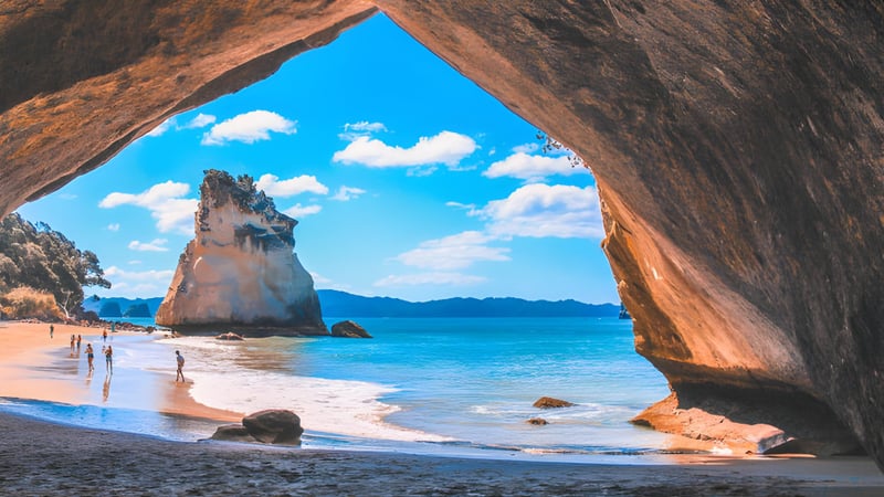 Ein natürlicher Felsenbogen zeigt die Küstenlandschaft mit Strand und Bergen nahe dem Newlands College.