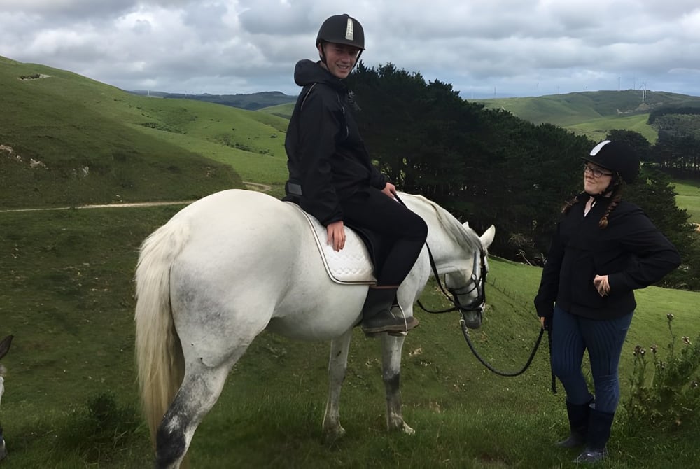 Eine Person reitet ein weißes Pferd auf einer hügeligen Wiese auf dem Gelände des Newlands College.