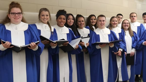 Eine Gruppe Schülerinnen der Newman Central Catholic High School steht im Flur mit blauen Abschlussroben und weißen Hemden zusammen.