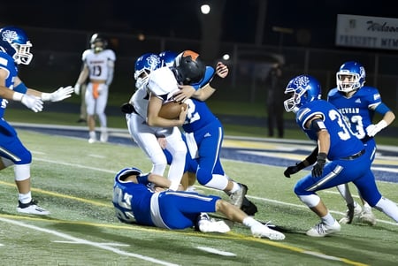 Spieler der Newman Central Catholic High School sind während eines Footballspiels in einem Tackle auf dem Spielfeld zu sehen.