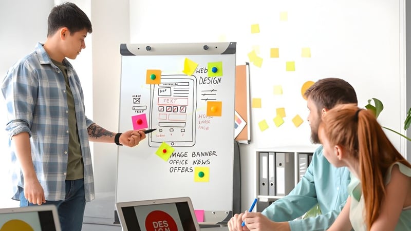 Zwei Personen arbeiten gemeinsam an einem Whiteboard bei einer Design-Session am Newman College.