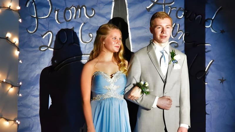 Ein junges Paar steht vor dem Dekor mit der Aufschrift Prom 2022 auf dem Campus der Newmarket High School.