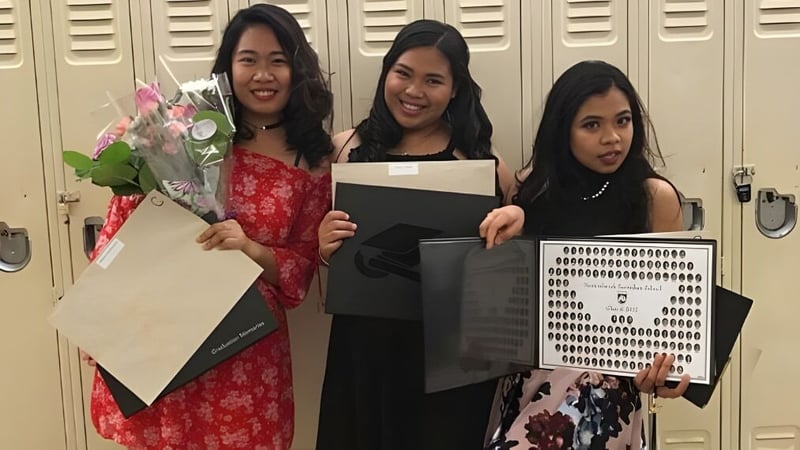 Drei Schülerinnen der Newtonbrook Secondary School stehen vor Schließfächern und halten Blumen sowie ein Plakat.