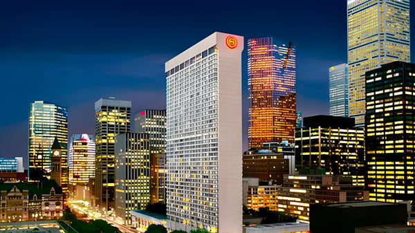 Ein Wolkenkratzer und weitere beleuchtete Hochhäuser sind bei Nacht vor dem Gebäude der Newtonbrook Secondary School zu sehen.