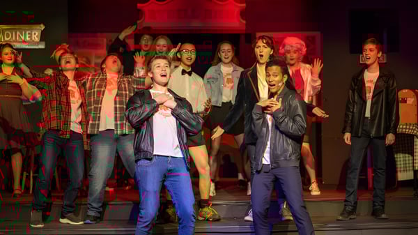 Eine Gruppe von Schülern der Newtown School steht auf einer Bühne mit rotem Hintergrund bei einer Veranstaltung.