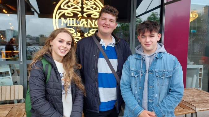 Drei Schüler der Newtown School stehen vor einem Café mit dem Schriftzug Milano.